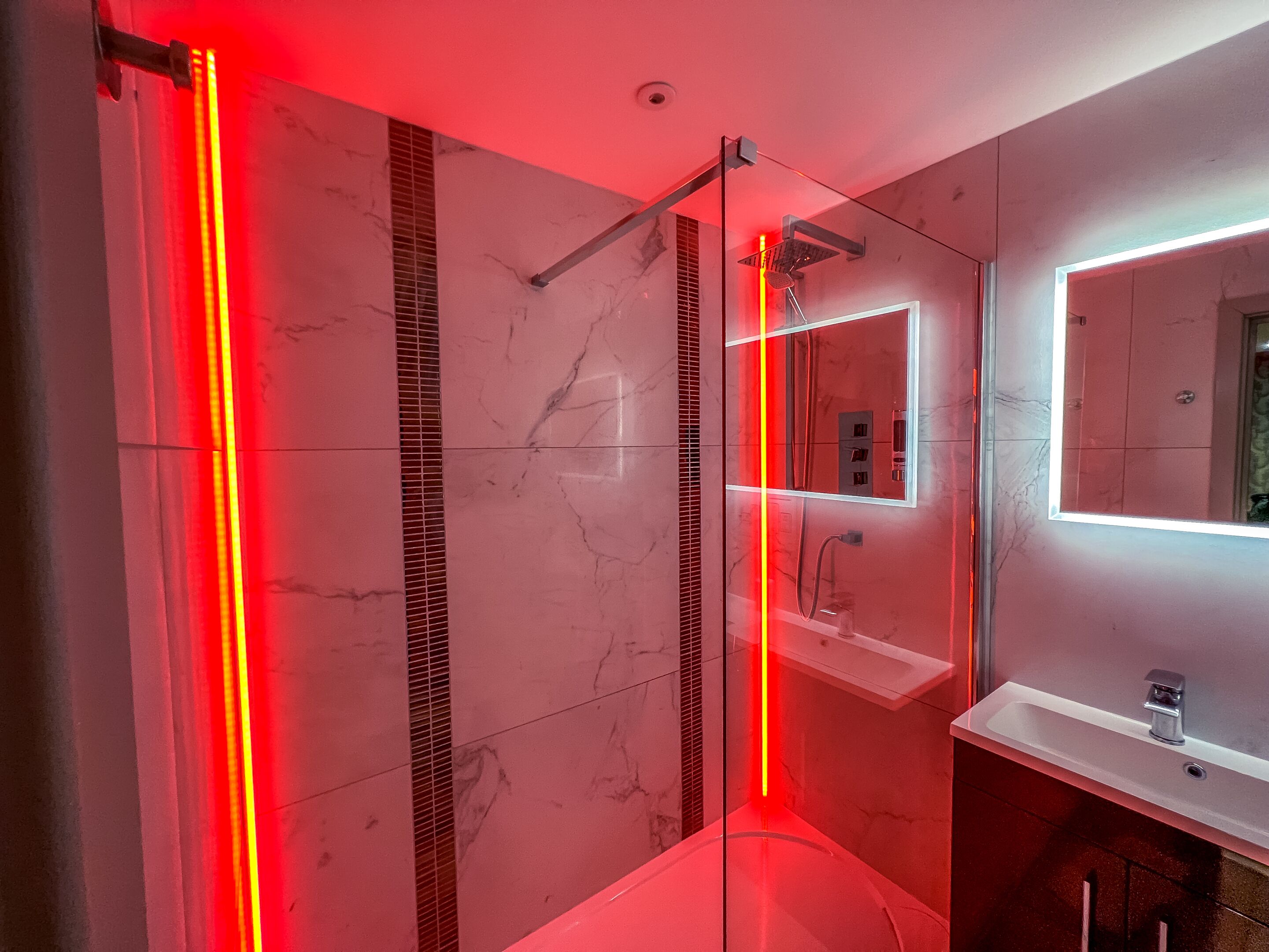 A modern bathroom with a glass-enclosed shower, a marble floor, and a large mirror above a white sink.