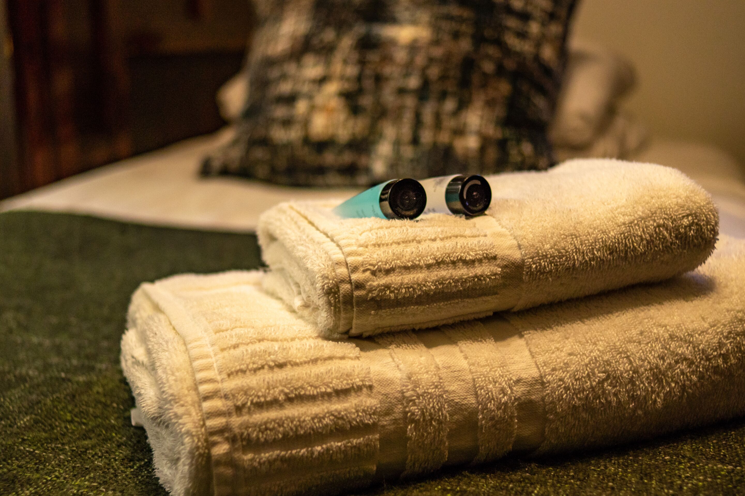 A neatly folded white towel with two black objects on top, placed on a green textured surface.