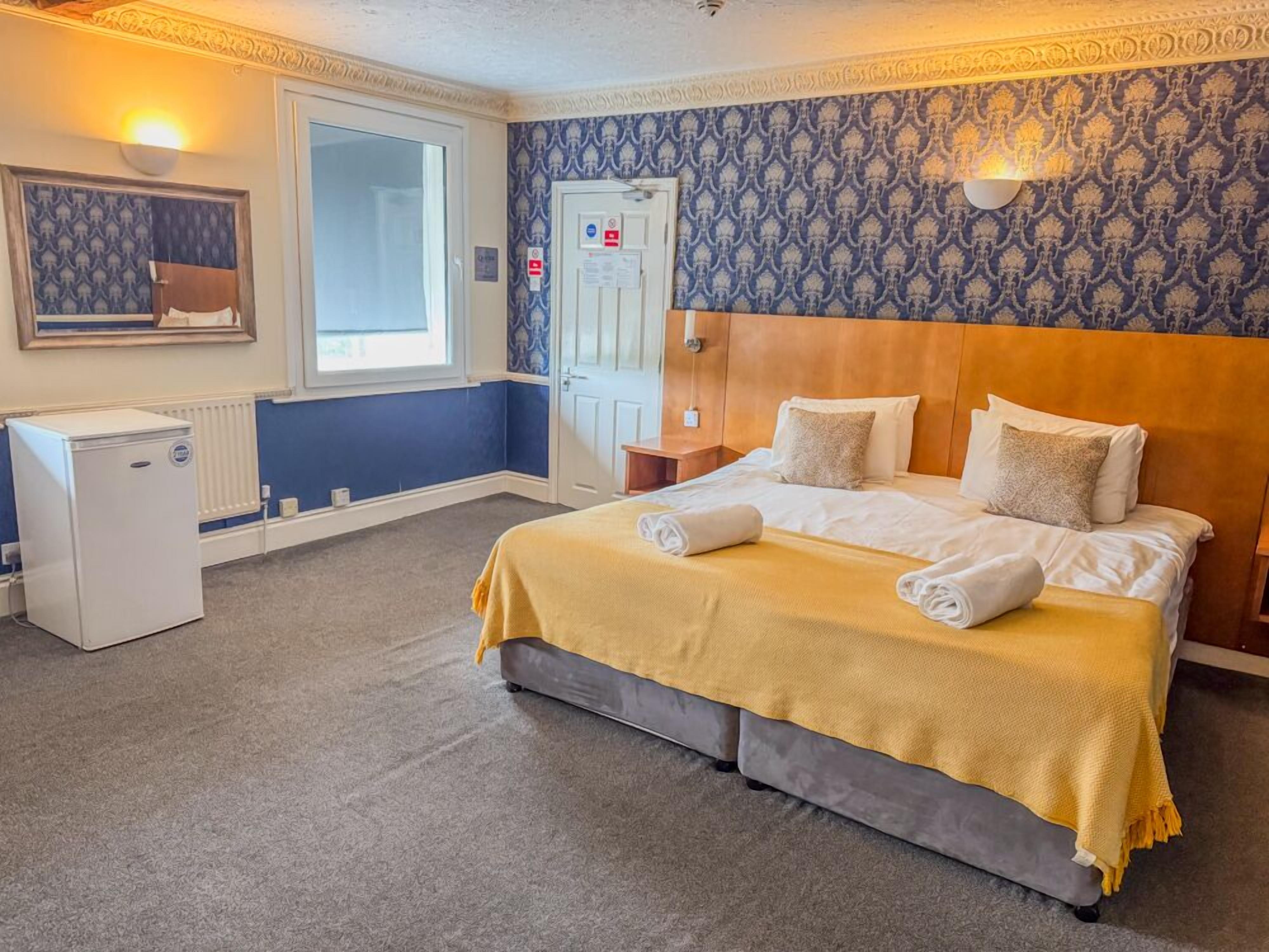 A hotel room with a bed, a small refrigerator, a window, and a door.