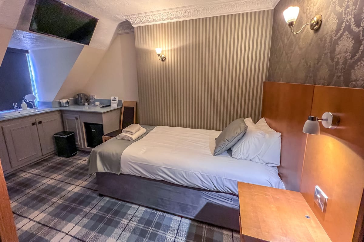 A hotel room with a bed, a small desk, a mirror, a sink, and a window.