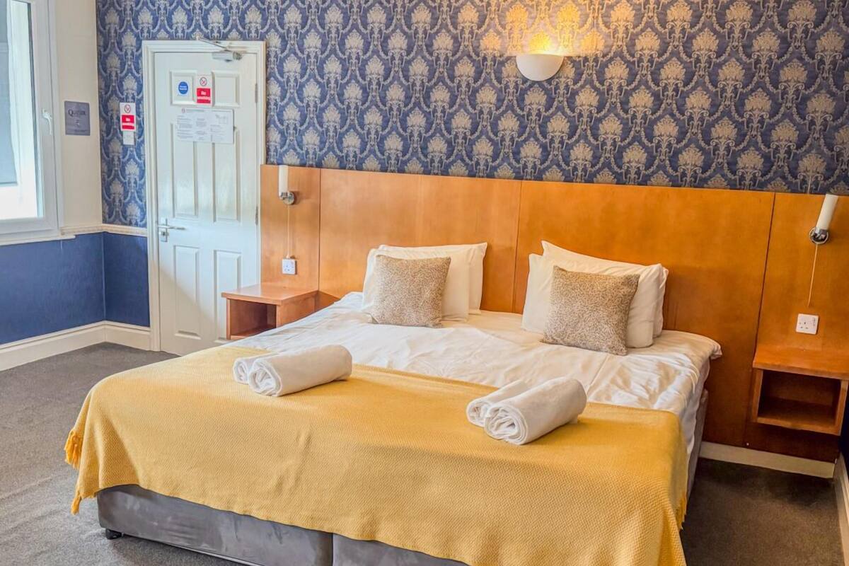 A hotel room with a large bed, a wooden headboard, and a patterned wallpaper.