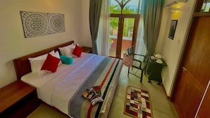 Une chambre d’hôtel avec un lit, une table de chevet, une chaise, une petite table avec un téléphone et une théière, et une vue sur la verdure à l’extérieur.