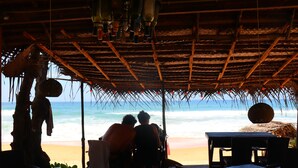 Un restaurant situé en bord de mer, avec un toit de chaume, des tables et des chaises en bois, et une vue sur l’océan.