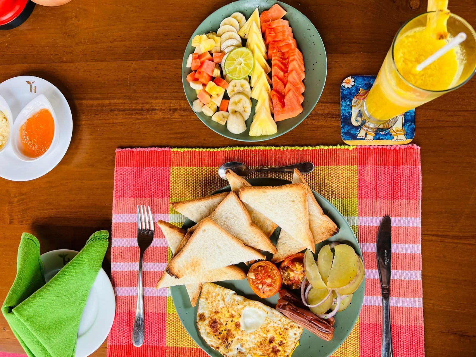 A breakfast setting with toast, eggs, tomatoes, and a variety of fruits on a table.