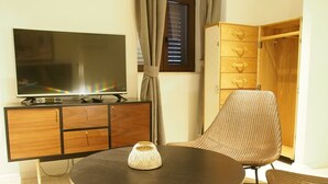 A modern living room with a flat-screen TV on a wooden cabinet, a round table with a decorative item, and a wicker chair. - Luxury Style Apartments (Dubrovnik)