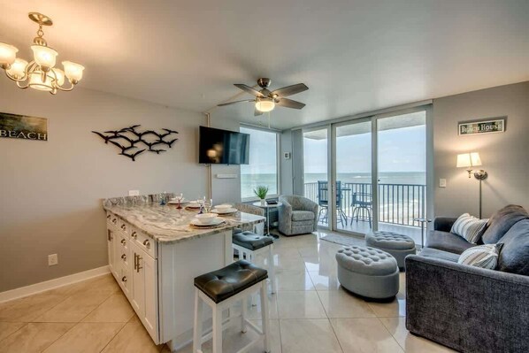 A modern kitchen with a marble countertop, a ceiling fan, and a dining area with a view of the beach.