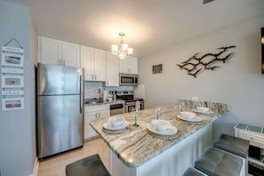 A modern kitchen with white cabinets, stainless steel appliances, a marble countertop, and a built-in island with seating.