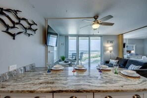 Une cuisine moderne dotée d’un plan de travail en marbre, d’un ventilateur de plafond et offrant une vue sur le balcon.
