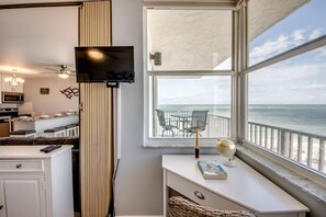 Une chambre dotée d’une télévision, d’un bureau avec un globe terrestre, d’une vue sur la mer et d’un balcon avec des chaises.