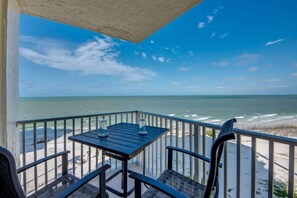 A balcony with a table and chairs overlooking a beach.