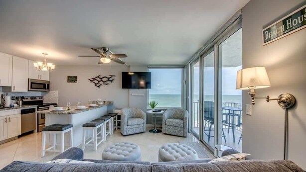 A modern kitchen with a dining area, a sofa, and a view of the ocean.