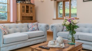A cozy living room with two light blue sofas, a wooden coffee table with a teapot, cups, and a remote control.