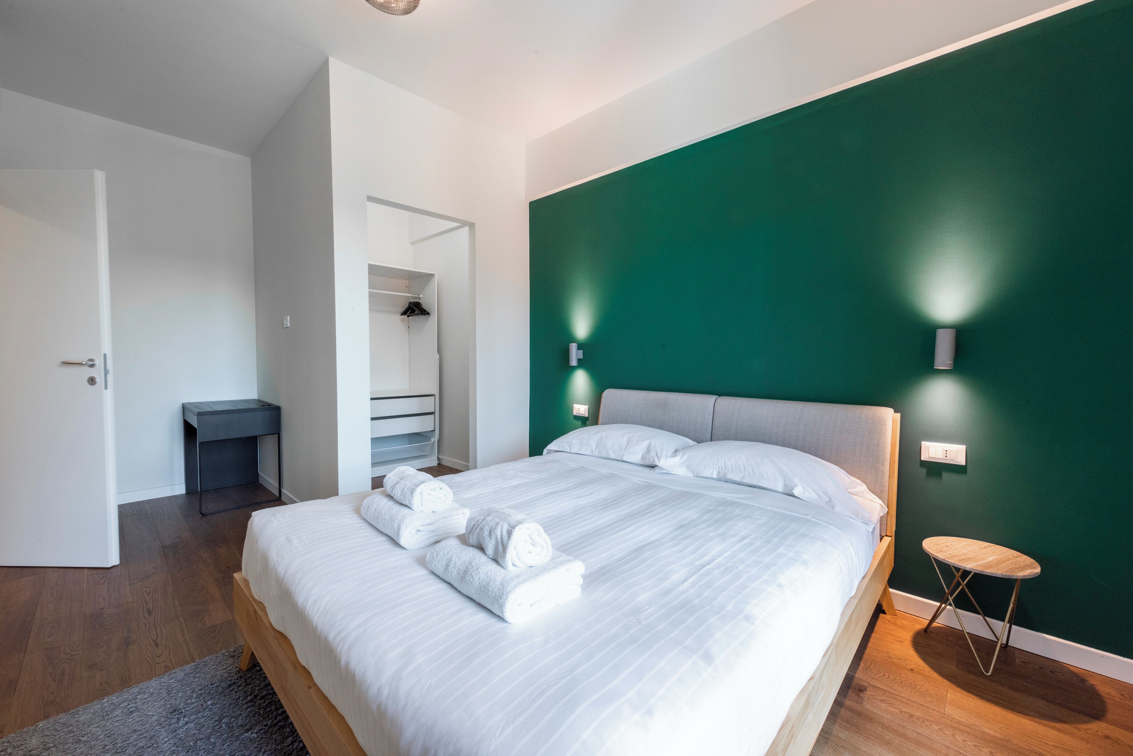 Ein modernes Schlafzimmer mit einem großen Bett, einem kleinen Nachttisch und einer Wand in Grüntönen.