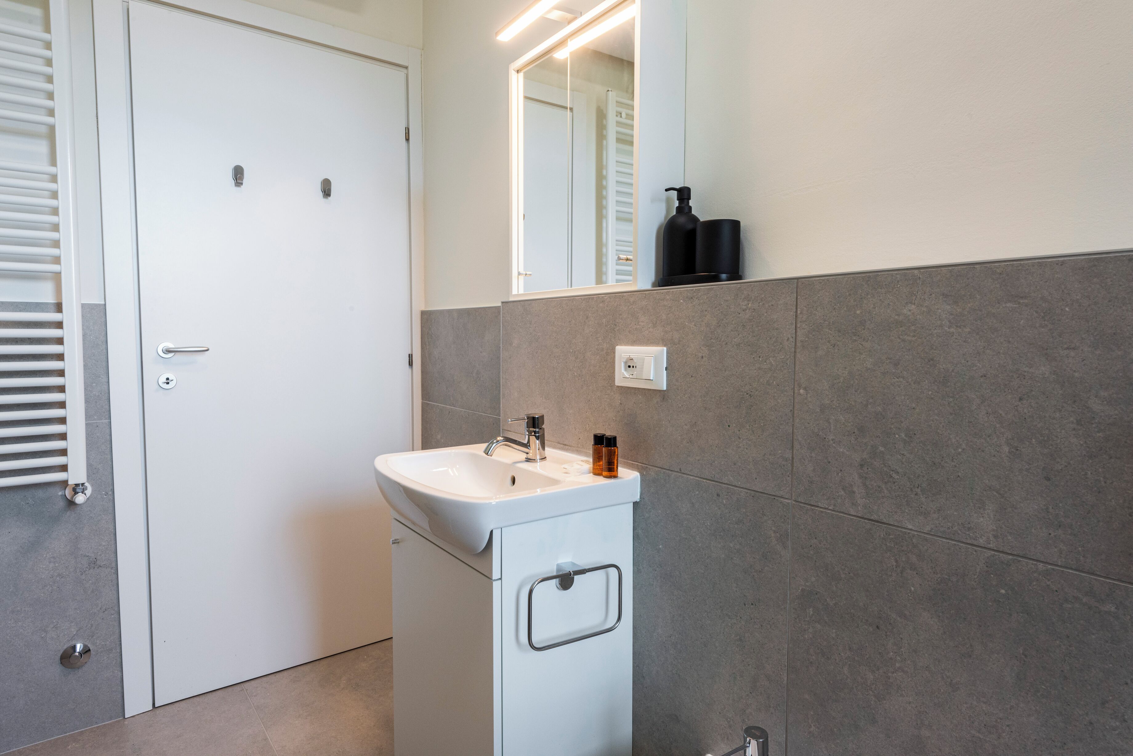 Un baño con lavamanos blanco, espejo y toallero.