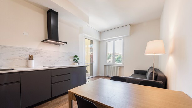 Une cuisine moderne avec des meubles de couleur sombre, un plan de travail en marbre et une hotte noire.