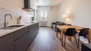 Une cuisine moderne dotée d’un plan de travail en marbre, d’un évier en acier inoxydable et d’une cuisinière encastrée. On y trouve également un coin repas avec une table en bois et des chaises noires.