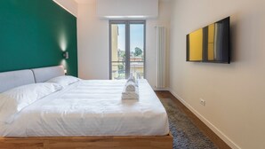 Une chambre d’hôtel moderne avec un grand lit, une vue sur la ville grâce à une porte coulissante et un téléviseur fixé au mur.