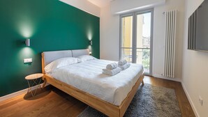 Une chambre à coucher avec un lit en bois, des murs verts, une petite table ronde et une vue sur l’extérieur, visible à travers une porte-fenêtre coulissante.
