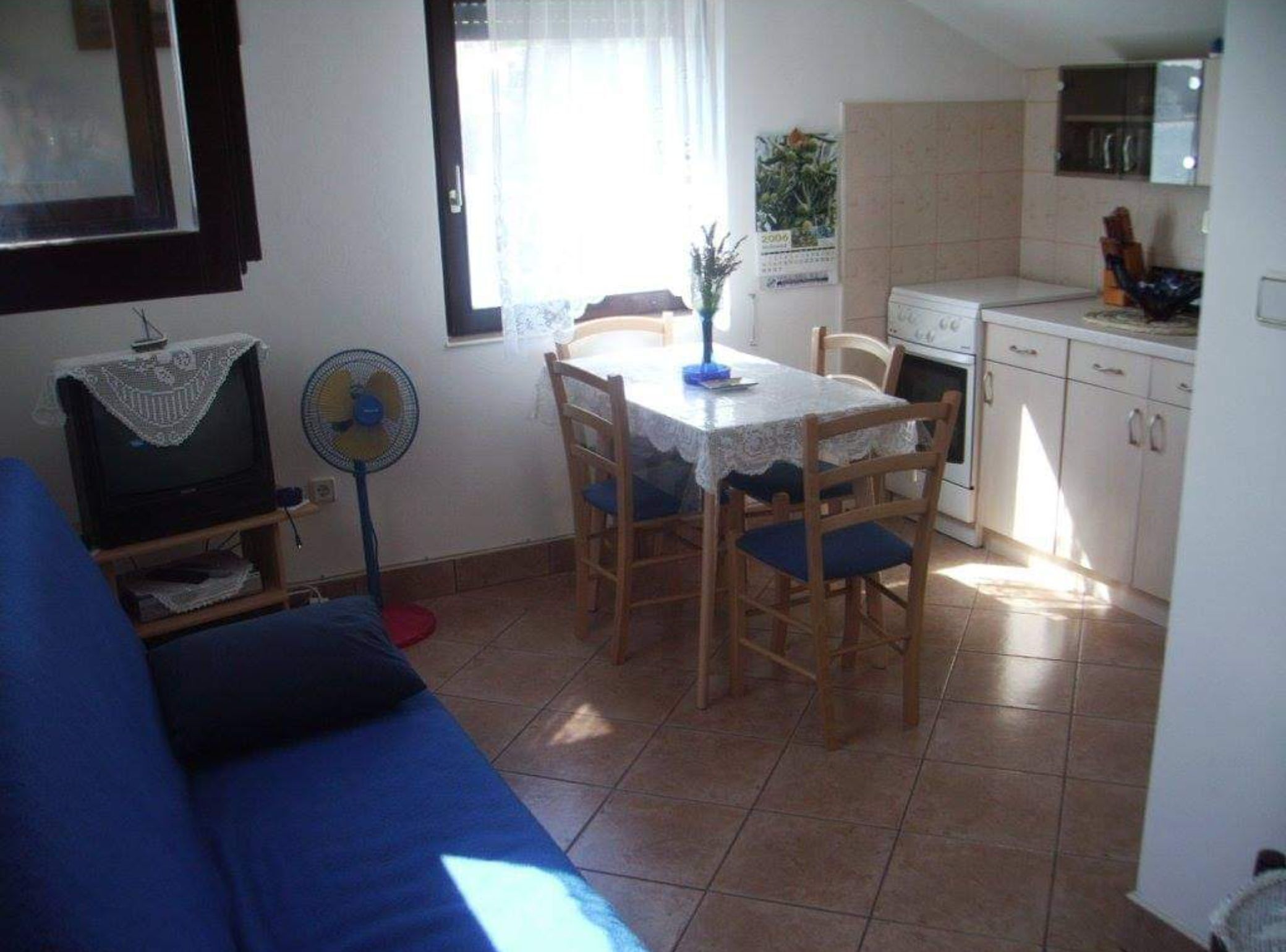 A compact living space with a dining table, chairs, a sofa, a TV, and a fan.