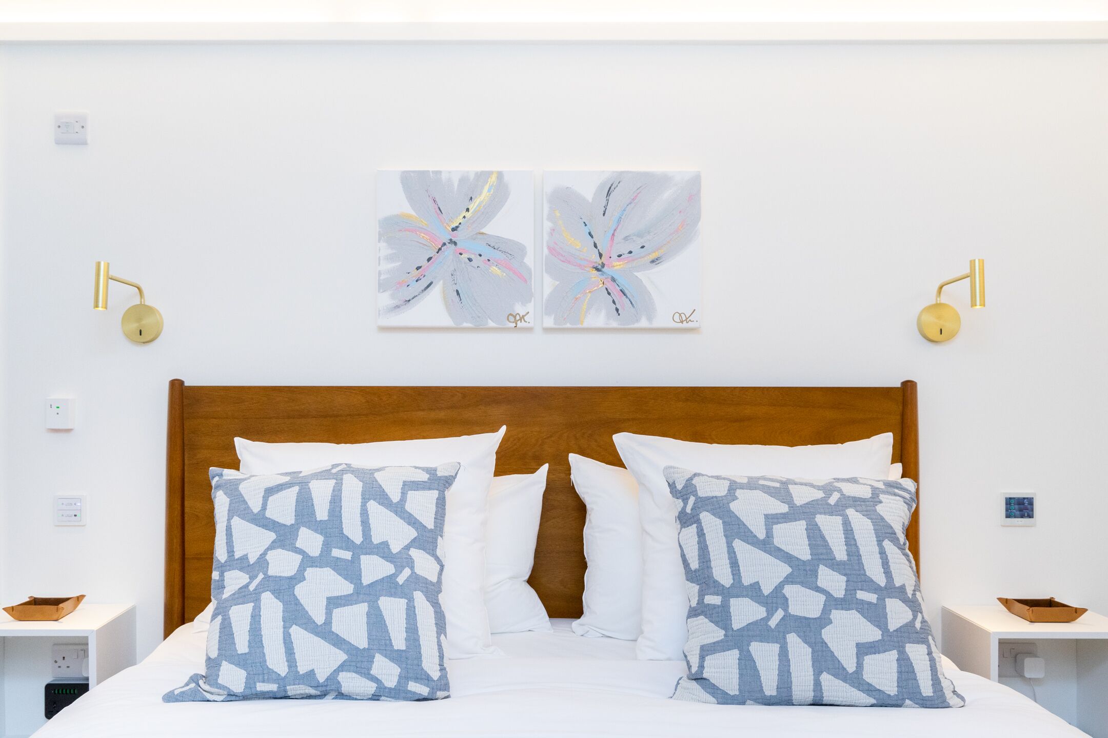 A neatly made bed with patterned pillows, a wooden headboard, and two wall-mounted lamps.