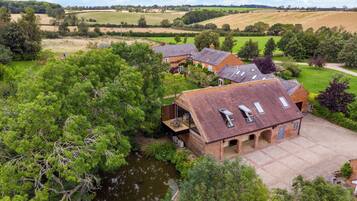 A modern house with a large patio, a pond, and a view of the surrounding countryside.