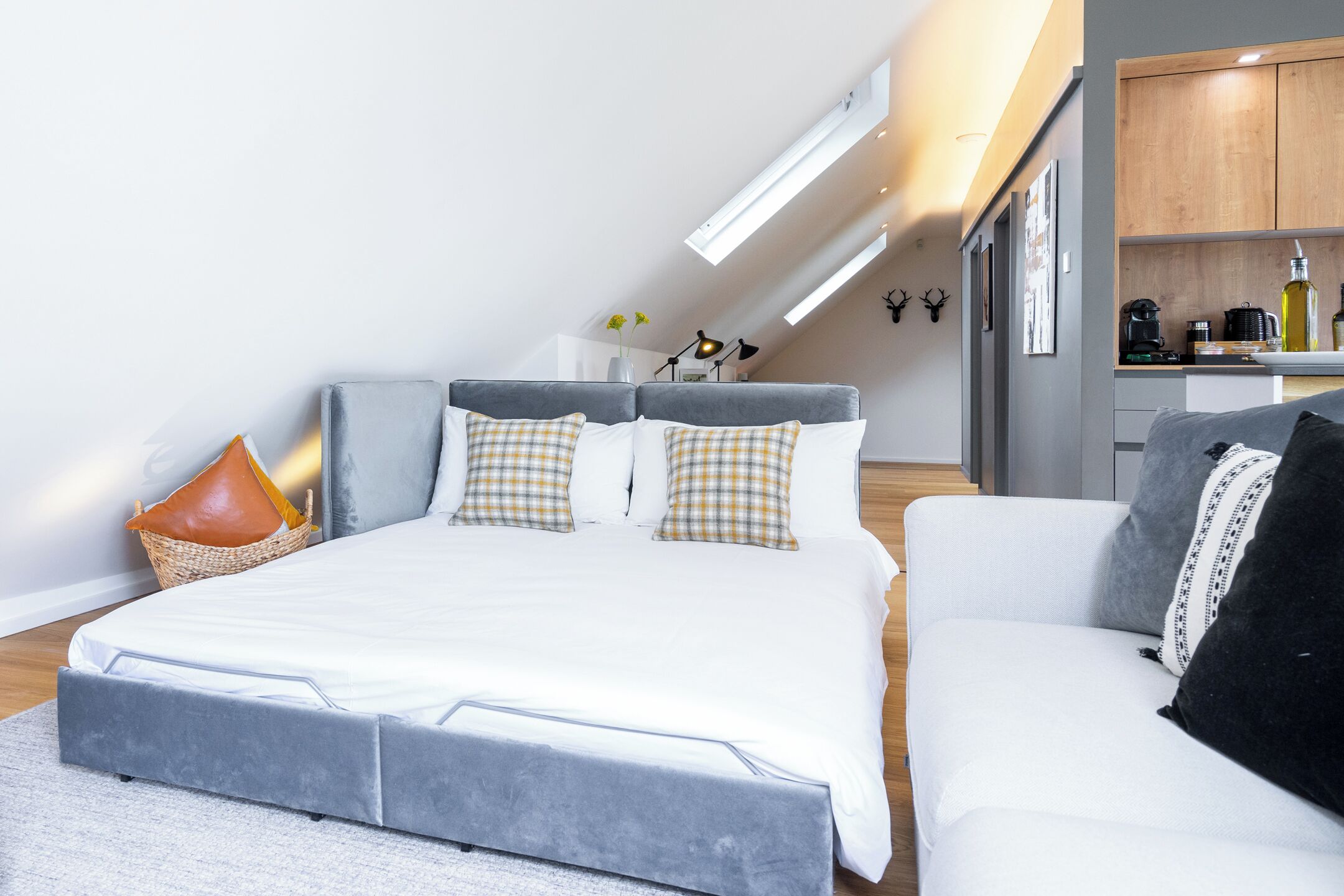 Un dormitorio moderno con una cama grande, un sofá, una pequeña cocina y un techo estilo loft.