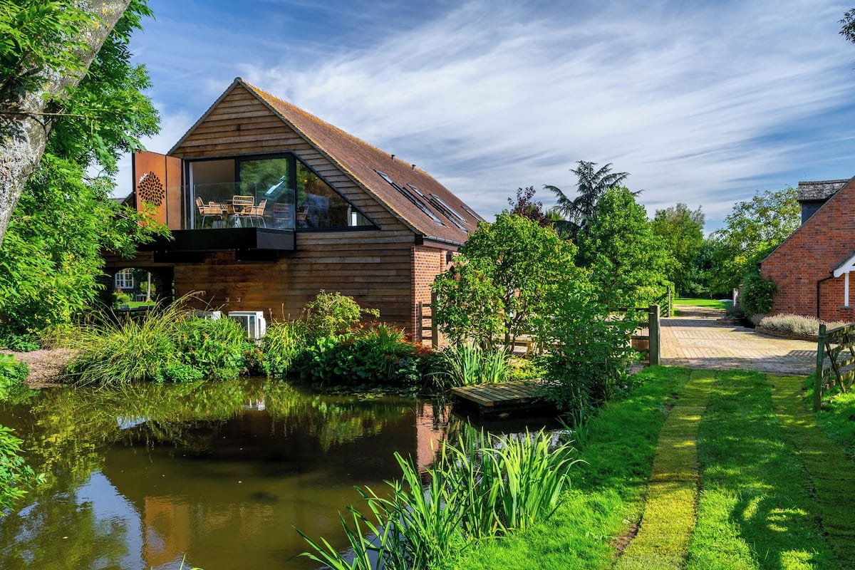 Ein modernes Haus mit Holzfassade, einem Glasbalkon und einem Teich im Garten.