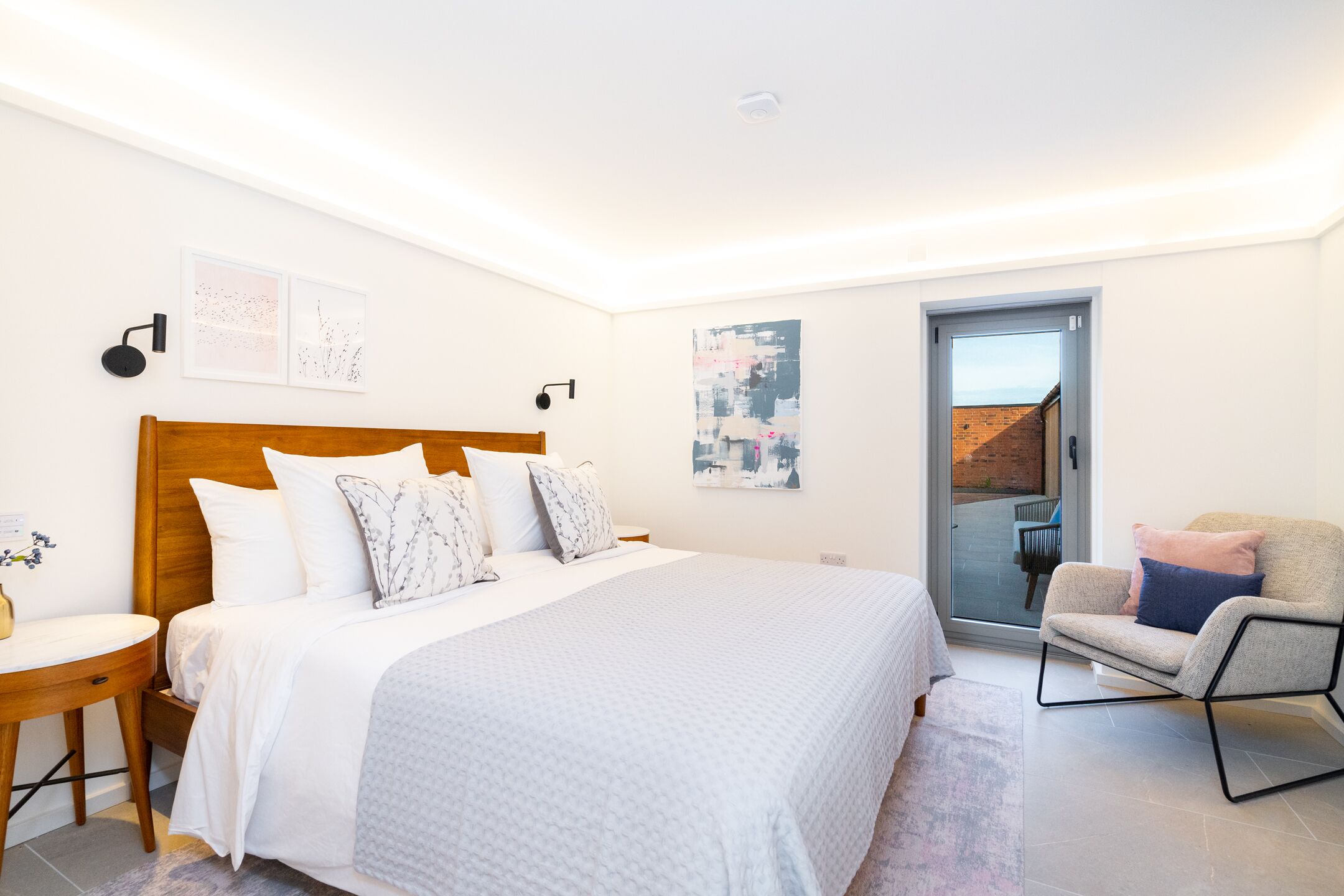 Ein Schlafzimmer mit einem großen Bett, einem Sessel, einem Schreibtisch und Blick ins Freie.