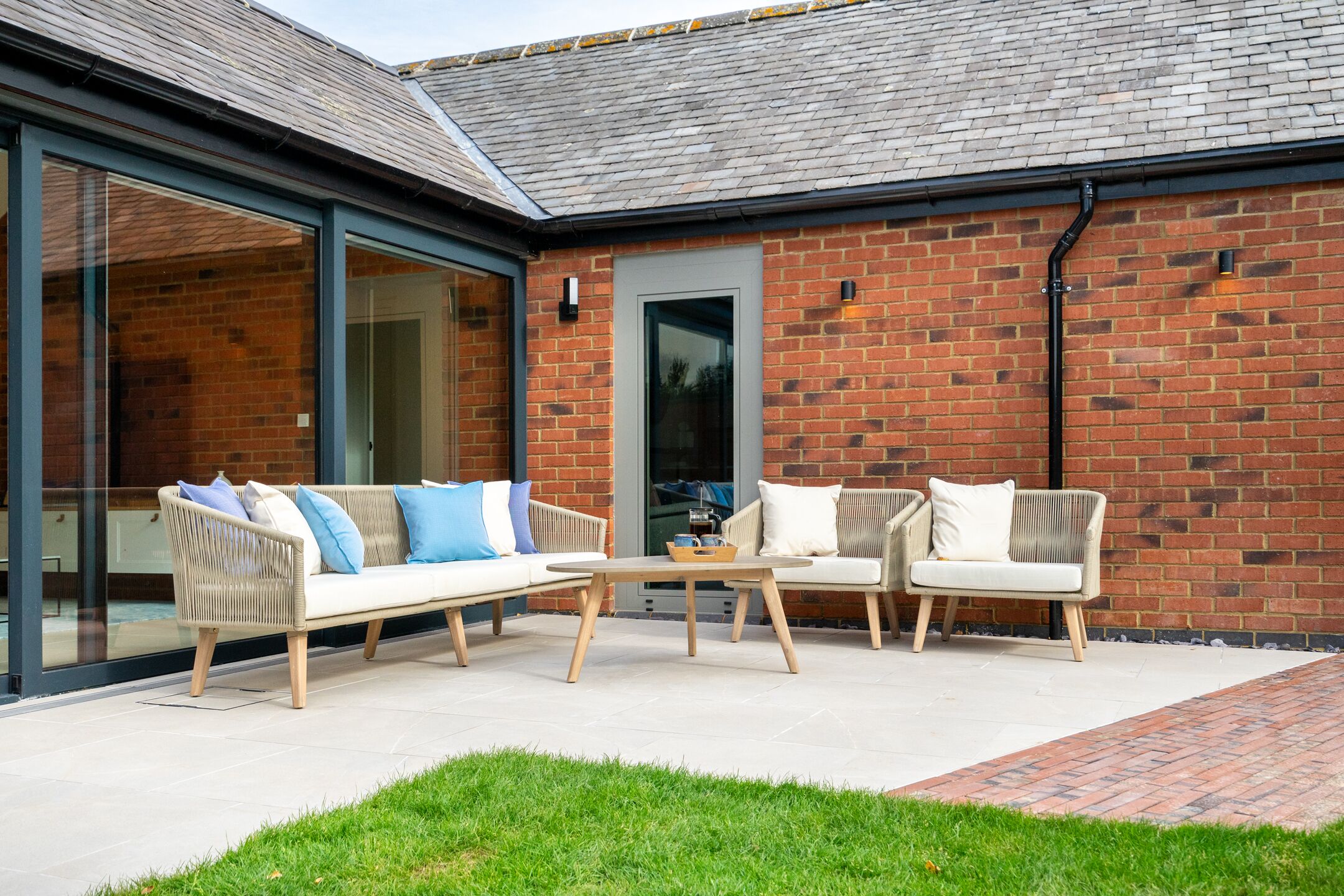 An outdoor seating area with two sofas and a coffee table, a brick wall, and a glass door leading to a patio.