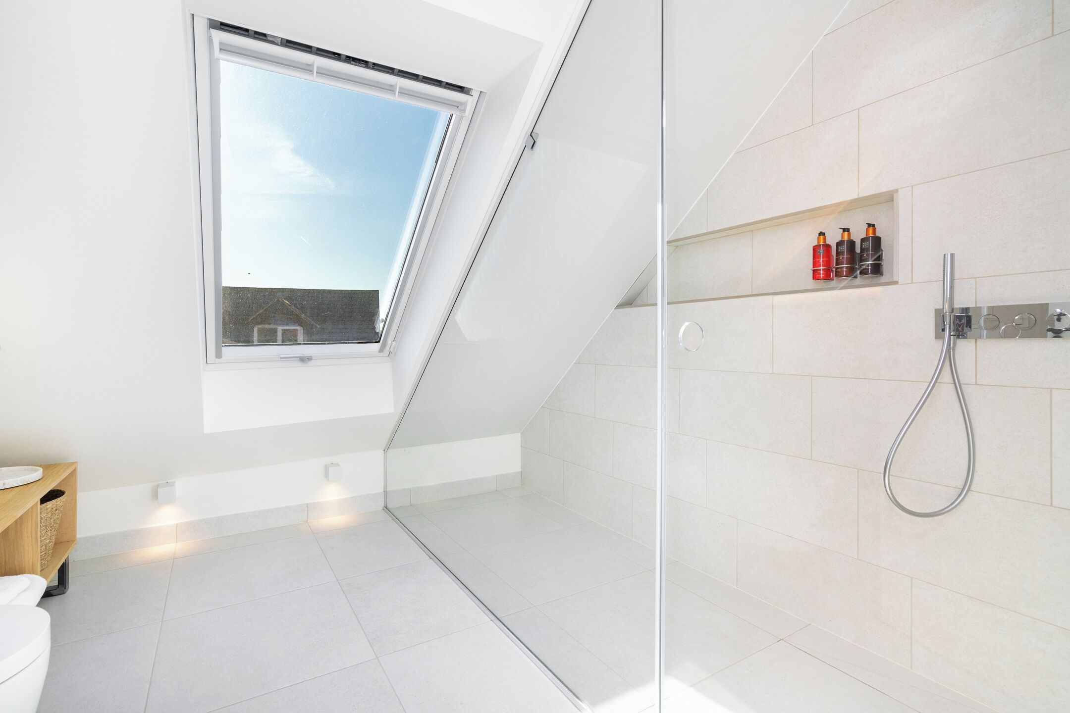 Un baño moderno con tragaluz, cabina de ducha de vidrio y estante con artículos de aseo.