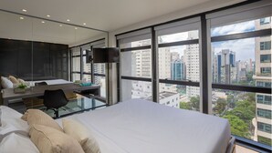 Una camera d'albergo moderna con un letto grande, una scrivania con una sedia, una televisione a schermo piatto e ampie finestre con vista sulla città.