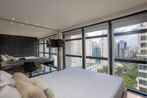 Een moderne hotelkamer met een groot bed, een bureau met stoel, een flatscreen televisie en grote ramen met uitzicht op de stad.