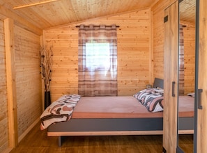 A wooden cabin room with a bed, a window with curtains, and a wooden floor.