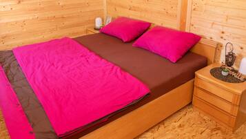 Ein holzgetäfeltes Zimmer im Blockhausstil mit einem Bett, rosa-brauner Bettwäsche, einem Nachttisch mit einer Laterne und einer kleinen Pflanze.