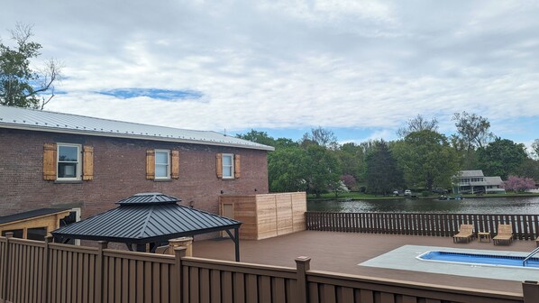 A deck with a pool, a wooden fence, and a brick building with windows.