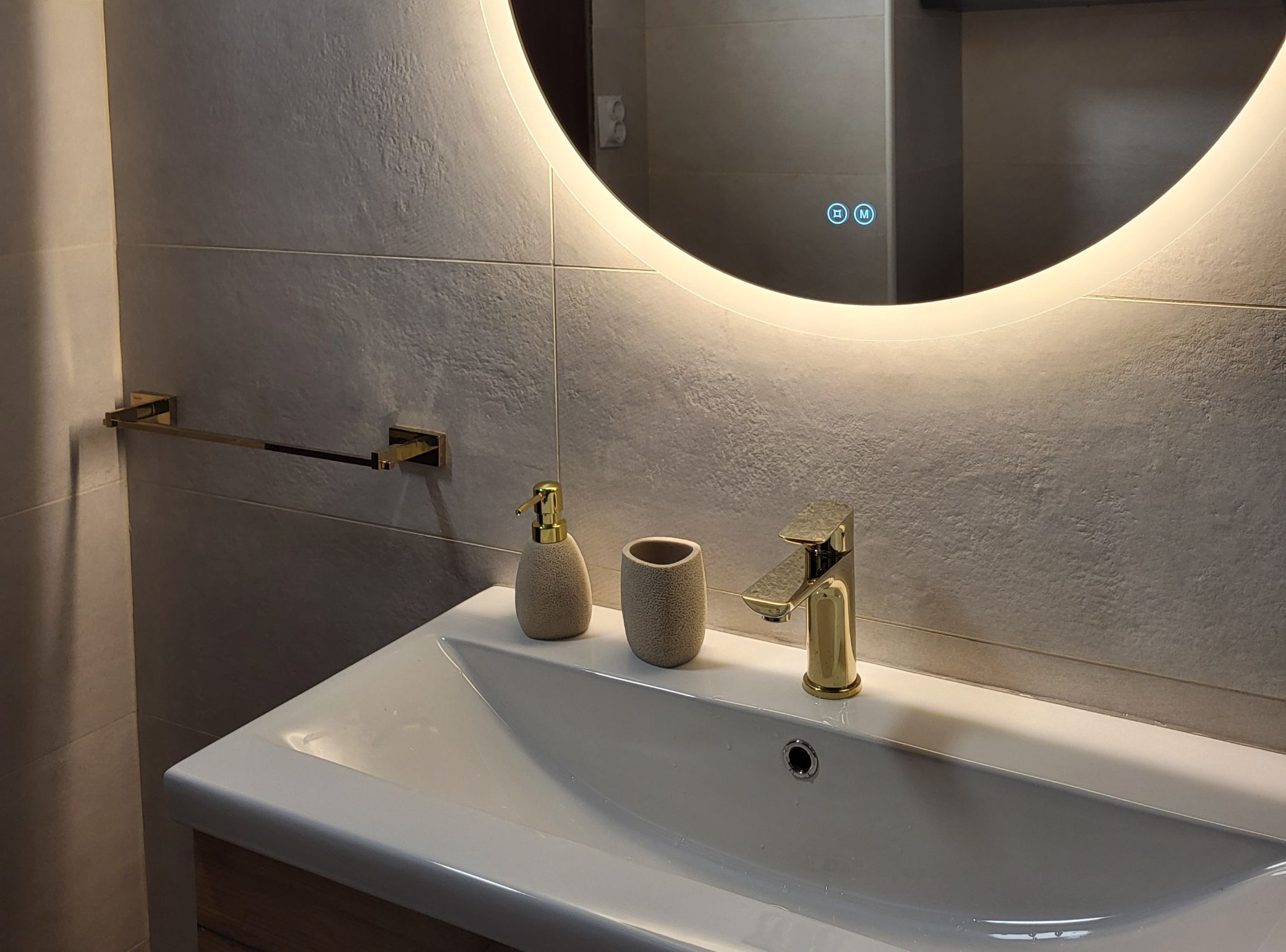 Un baño con lavamanos blanco, grifo dorado, dispensador de jabón y barra para toallas.