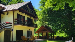 Um edifício de dois andares com varanda, área de estar coberta ao ar livre e mesa de jantar com cadeiras.