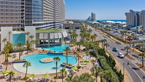 Een hotel met een groot zwembad, palmbomen en uitzicht op het strand.