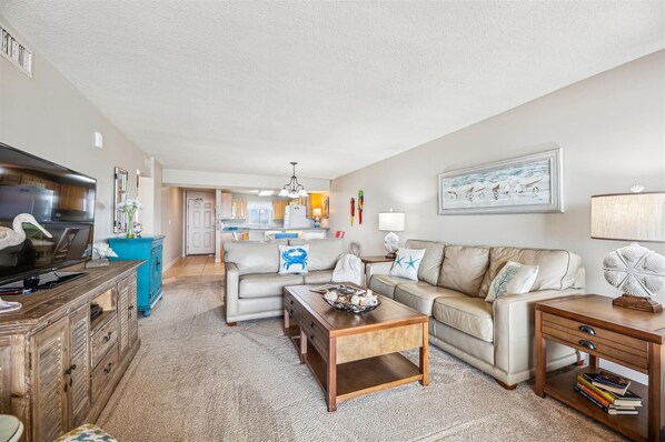 A spacious living room with a sofa, coffee table, and a TV. There is a kitchen in the background and a dining area. - NEW LISTING! Sandy Key 436 4th floor -Beachfront view -NO HASSLE CHECK OUT (Pensacola)