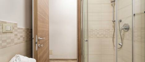 A modern bathroom with a glass shower enclosure, a wooden door, and a white sink with a towel.