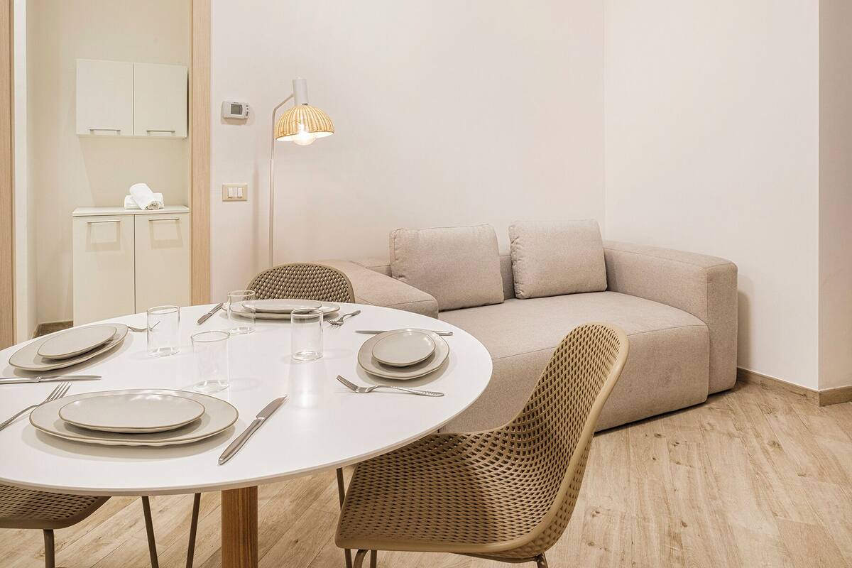 A dining area with a round table set for four, a sofa, and a lamp.