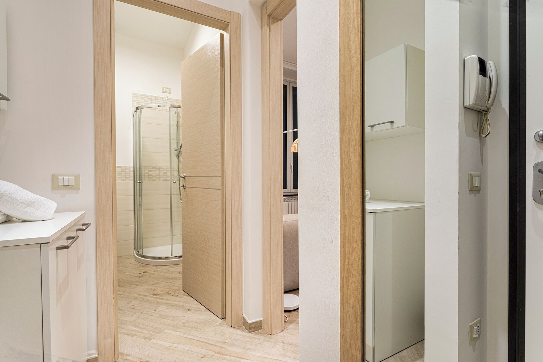 A narrow hallway leading to a bathroom with a glass shower enclosure, a white sink, and a towel on the counter.