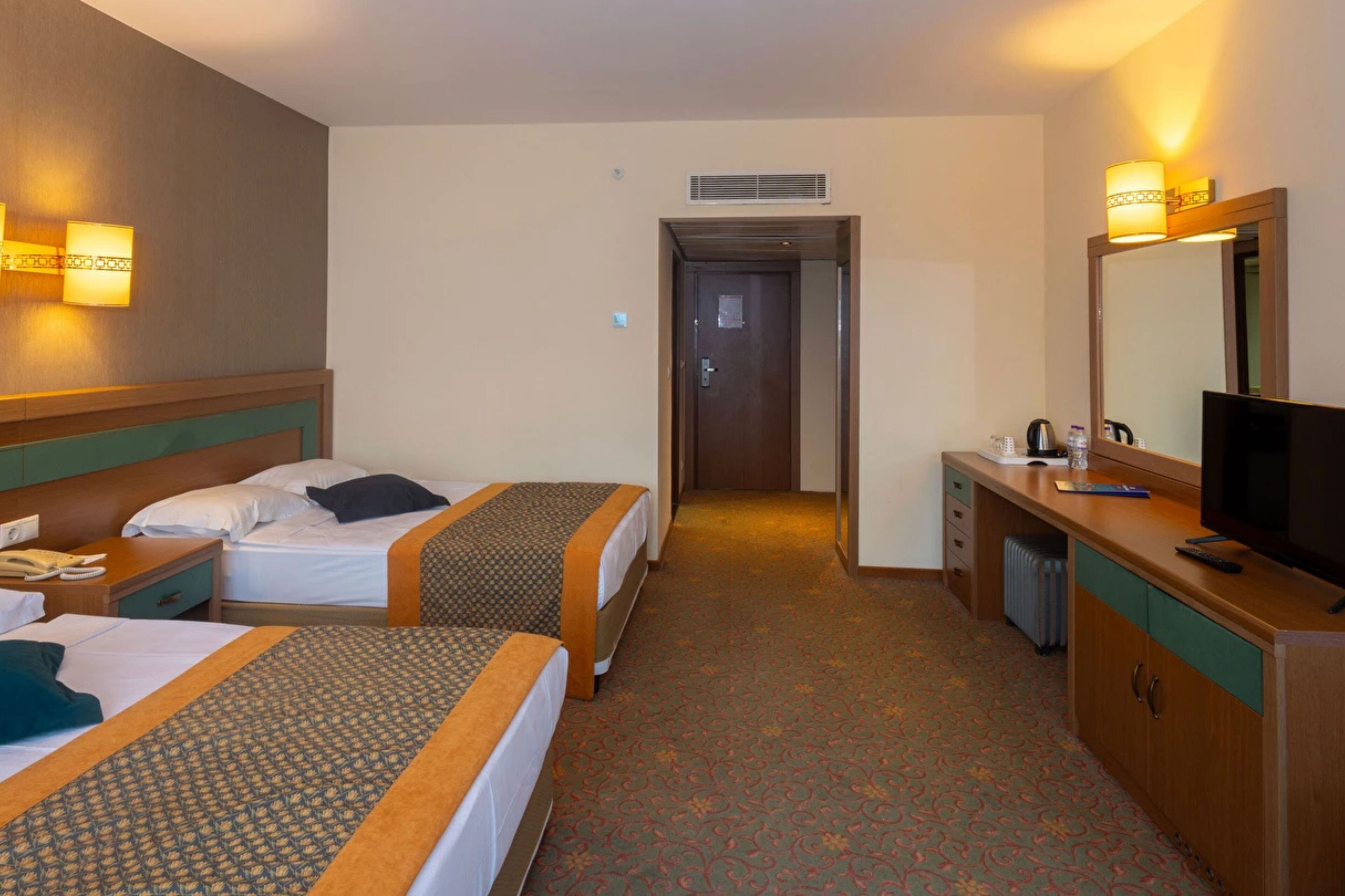 A hotel room with two beds, a desk, a television, and a mirror.