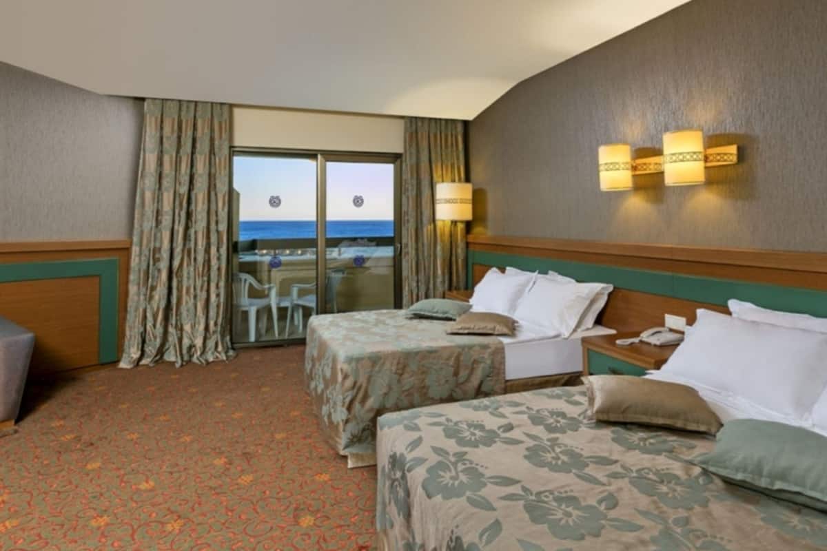 A hotel room with two beds, a view of the ocean through a sliding door, and a small table with chairs.