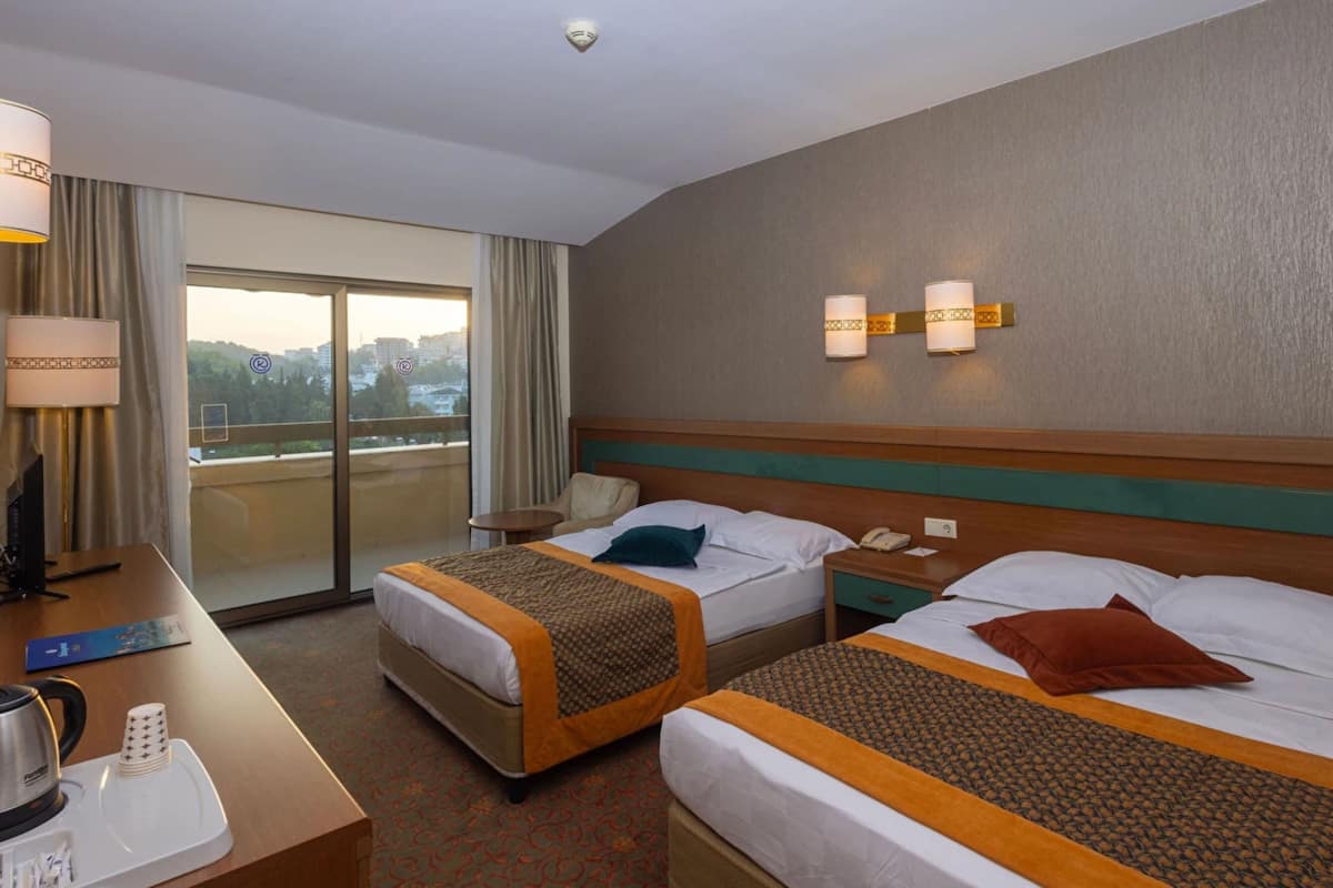 A hotel room with two beds, a desk with a coffee maker, a telephone, and a view of the city through the window.