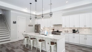 A modern kitchen with white cabinetry, a central island with bar stools, stainless steel appliances, and pendant lighting. - Close to 2 Beach Accesses on 30A! Golf Cart, Large Private Pool and Hot Tub (Santa Rosa Beach)