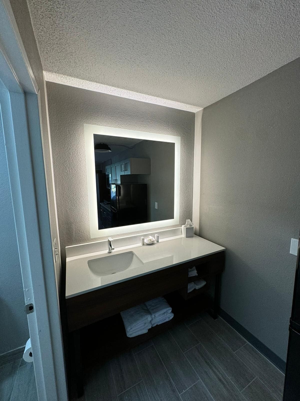 A modern bathroom with a large mirror, white sink, and dark vanity.