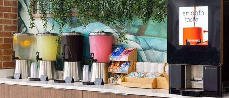 A beverage station with multiple dispensers and a coffee machine, surrounded by a counter with various items and a mural in the background.