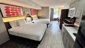 Habitación de hotel con dos camas, kitchenette, televisor y obras de arte en las paredes.