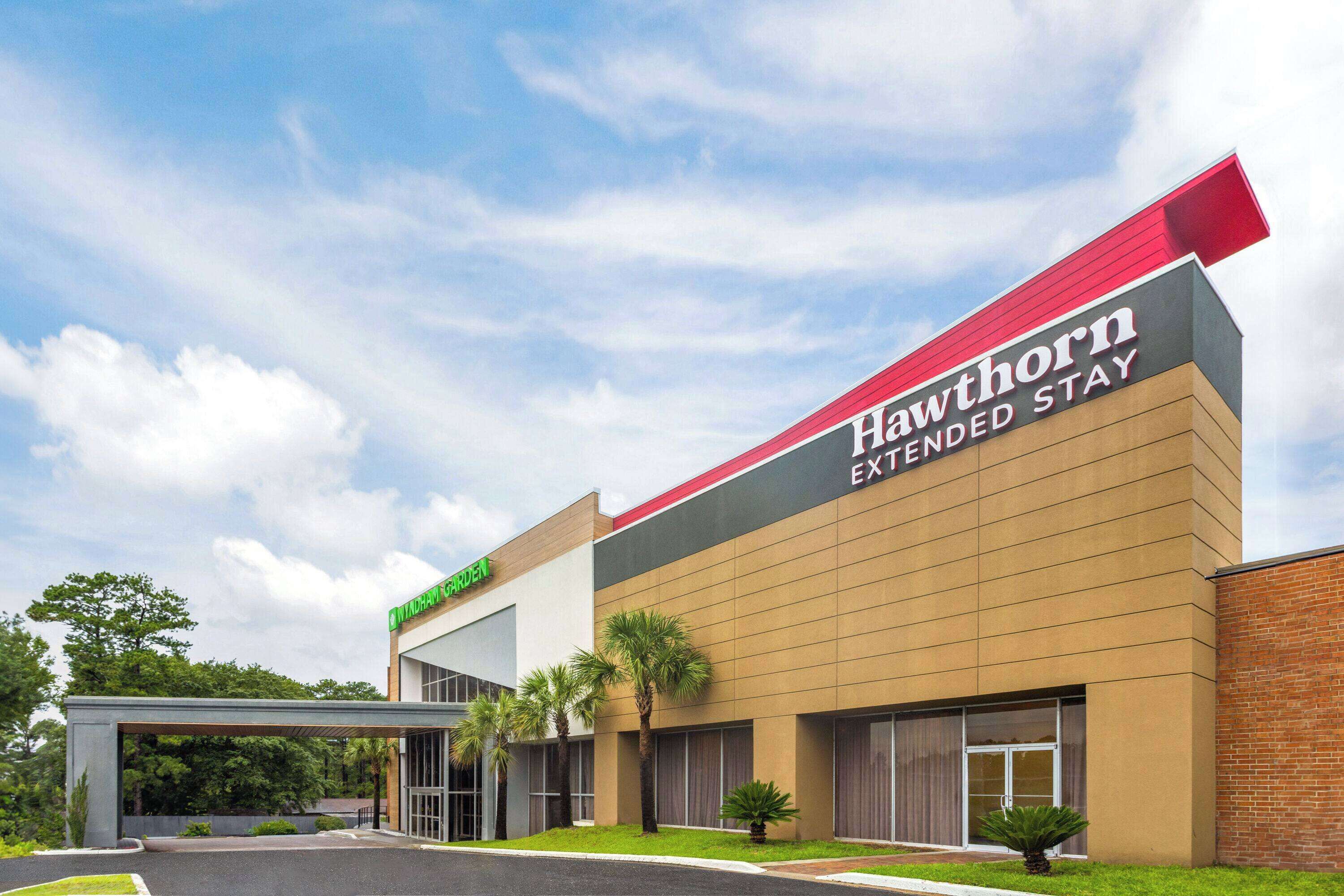 Un hotel Hawthorn Extended Stay con un diseño moderno, que destaca por su techo rojo y una entrada con jardín.